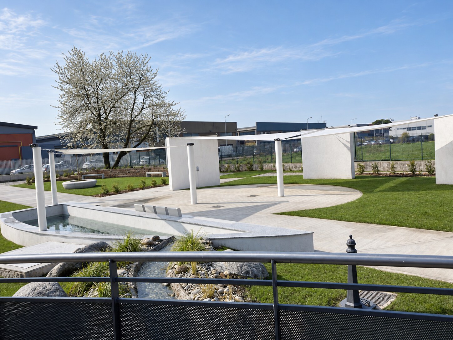 Vista generale del giardino sensoriale con acqua, percorsi, prato e strutture ombreggianti